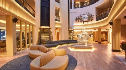 Modern hotel lobby with circular beige seating, abstract sculpture, wooden floors, and warm ambient lighting.