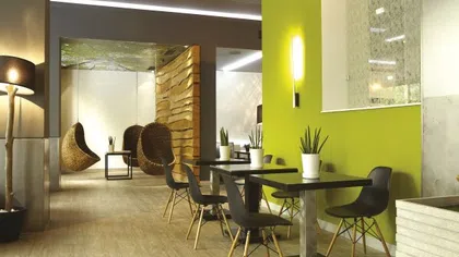 Modern indoor seating area with black chairs, tables, potted plants, wooden floor, and hanging woven chairs in background