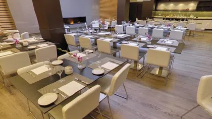 Modern restaurant interior with neatly arranged tables, white chairs, and elegant table settings.