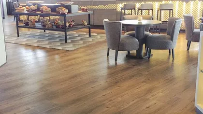 Modern cafe interior with wooden flooring, round tables, cushioned chairs, and a food display counter with various pastries.