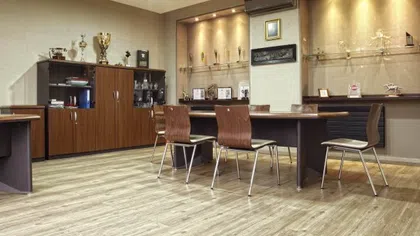 Modern office room with wooden chairs, trophies on shelves, display cabinets, and warm overhead lighting.