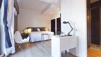 Bright modern bedroom with white walls, a queen bed, desk with lamp, and open closet space
