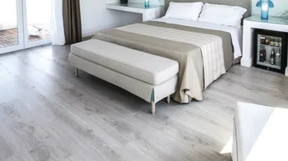 Modern bedroom with a double bed, beige bench, light wood flooring, and natural light from sliding doors.