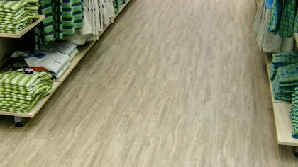 Wooden laminate flooring in a retail store aisle with folded green and beige clothing on shelves.