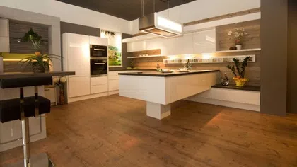 Modern kitchen with white cabinetry, floating island, wood flooring, and contemporary lighting fixtures
