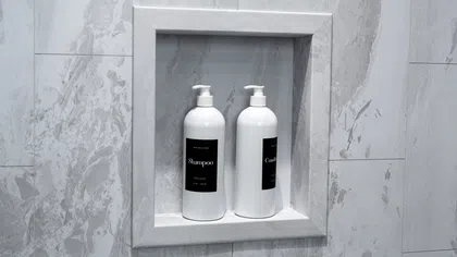 White shampoo and conditioner bottles with black labels in a marble shower wall niche