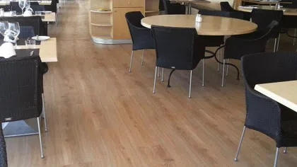 Modern restaurant interior with wooden floors, round and square tables, and black wicker chairs.