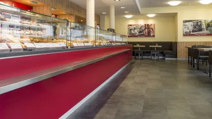 Modern bakery interior with glass display cases filled with pastries and seating area in the background
