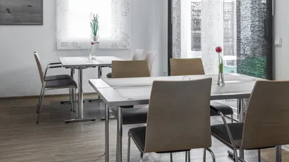 Modern dining area with wooden chairs, metal tables, minimalist décor, and light filtering through patterned curtains.