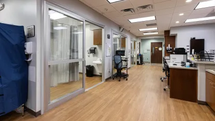 Modern medical clinic hallway with wood flooring, exam rooms, office chairs, and reception desk.