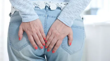 Woman in light blue jeans holding lower back with both hands showing red nail polish