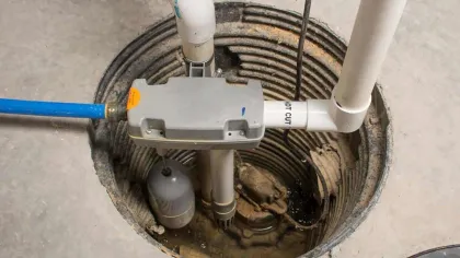 Basement sump pump system installed in a concrete pit with pipes and a float switch for water removal.