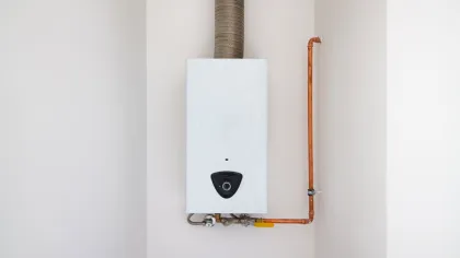 White tankless water heater mounted on wall with copper pipes and exhaust vent pipe.