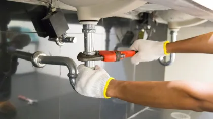 Plumber wearing gloves using a wrench to tighten pipes under a sink in a bathroom or kitchen