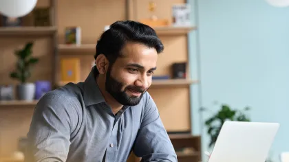 Smiling man working on laptop in a modern office with books and plants in the background