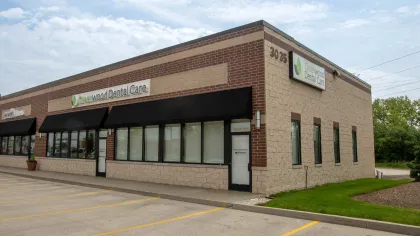 Exterior view of Greenwood Dental Care in a brick and stone building with black awnings and parking spaces in front.