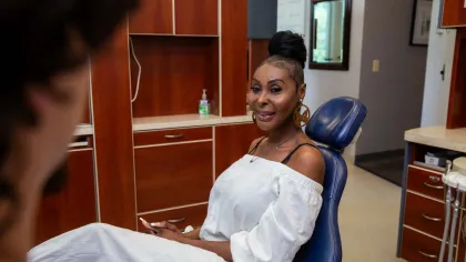 Woman in white outfit sitting in a dental chair smiling at the dentist in a clinic room