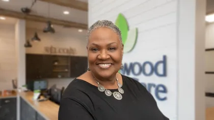 Smiling woman with short gray hair wearing a black top and silver necklace in a modern office lobby.