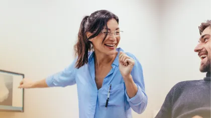 Smiling female dentist in blue shirt pointing at dental X-ray while patient in chair laughs