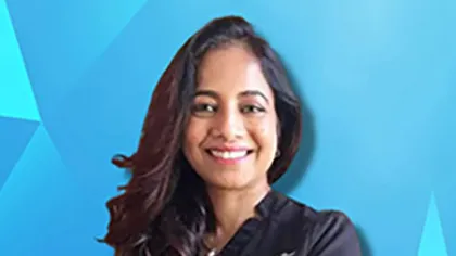 Smiling woman with long dark hair wearing a black top against a blue geometric patterned background