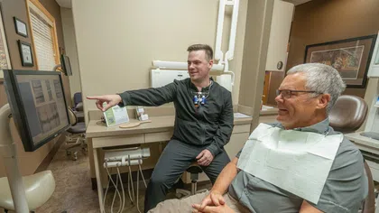 Dentist showing dental x-rays to smiling middle-aged male patient in dental office examination room