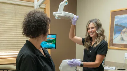 Dental hygienist adjusting overhead light in dental office while smiling at patient sitting in chair.