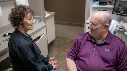 Female healthcare professional talking to a seated male patient in a medical office consultation.