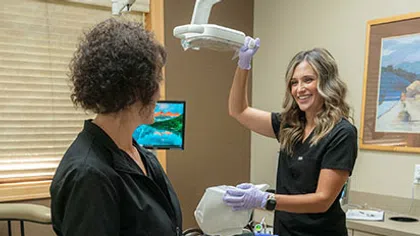 Dental hygienist adjusting overhead light in dental office while smiling at patient sitting in chair.
