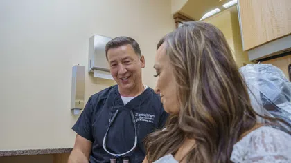 Dentist in black scrubs explaining a dental mold to a female patient in a clinic setting