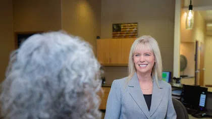 Professional woman in gray blazer smiling and interacting with a client in an office setting.