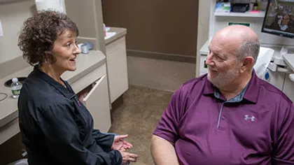 Female healthcare professional talking to a seated male patient in a medical office consultation.