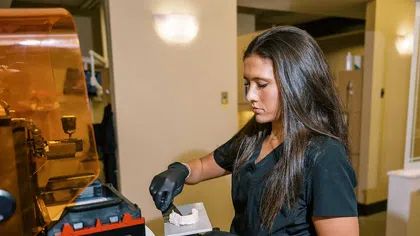 Dentist in black scrubs using dental 3D printer to create a dental mold model in clinic