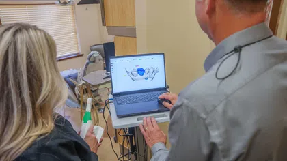 Dentist and assistant reviewing a 3D digital dental scan on a laptop in a dental office.