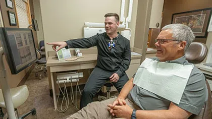 Dentist showing dental x-rays to smiling middle-aged male patient in dental office examination room