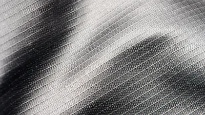 Close-up of textured gray fabric with fine woven patterns and light shadows creating depth and gradient.