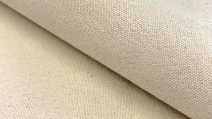 Close-up of natural beige cotton canvas fabric with visible weave texture rolled over flat surface