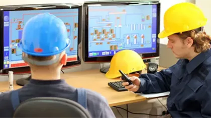 Engineers in hard hats monitoring industrial processes on computer screens in a control room.