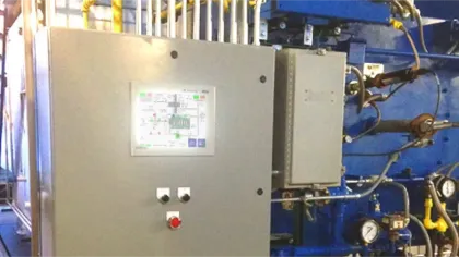 Industrial control panel with buttons and schematic display mounted on machinery with pipes and gauges.