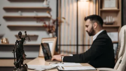 Lawyer working on laptop in office with Lady Justice statue and legal documents on desk