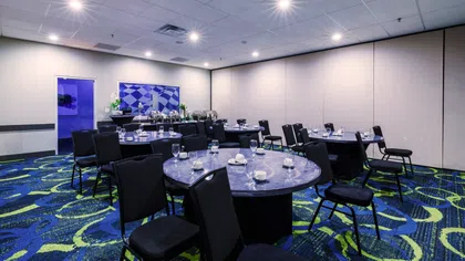 Conference room with round tables set with glassware and cups, blue patterned carpet, and soft ceiling lights.