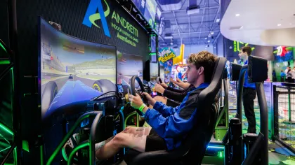 Young man focused on driving simulator at indoor gaming arcade with bright screens and neon lights