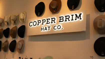 Copper Brim Hat Co. sign with various hats displayed on the wall in a warm, inviting store interior.