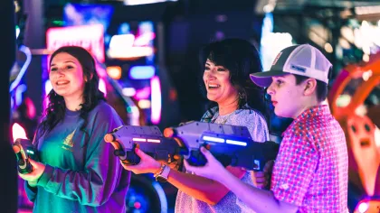 Three people enjoying a laser tag game in a colorful arcade filled with neon lights.