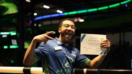 Happy employee holding Employee of the Month certificate, celebrating at a vibrant indoor sports venue.
