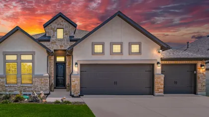 Modern house with stone and beige facade under a colorful red and purple sunset sky with lights on inside.