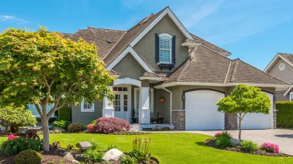 Modern suburban house with manicured lawn, two decorative trees, flower beds, and clear blue sky