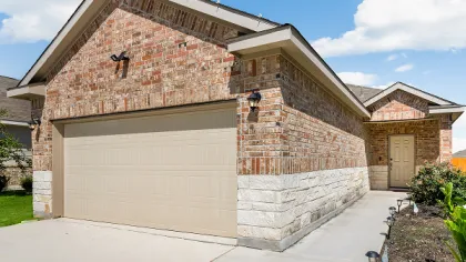 Brick and stone house with beige garage door on a sunny day with blue sky and white clouds.