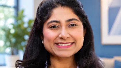 Confident female healthcare professional in white coat smiling with arms crossed in a modern office setting.