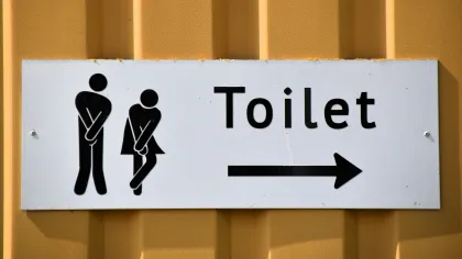 White sign with restroom figures and arrow pointing right on yellow wall indicating toilet direction.