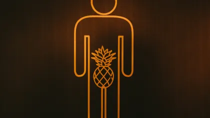 Orange neon outline of a person with a pineapple symbol in the groin area on a dark background.